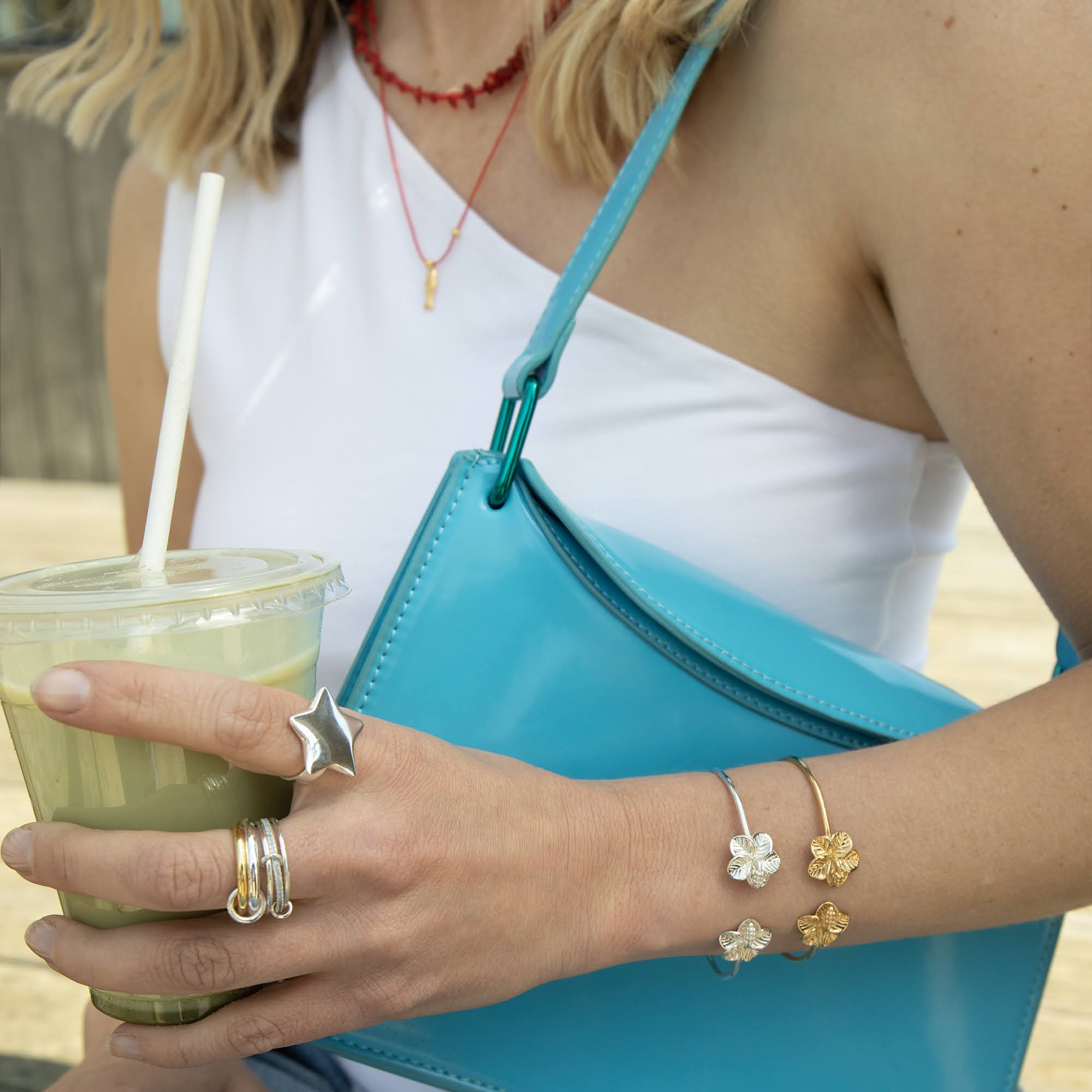 Person holding an iced matcha drink with a straw and a blue handbag, wearing multiple rings and bracelets - seolgold