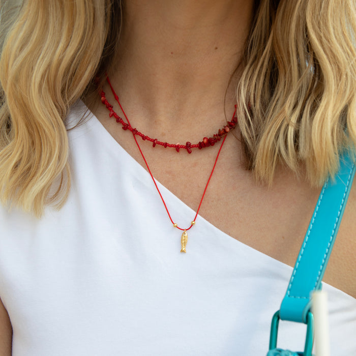 Person wearing a red beaded necklace with a small pendant, white top, and blue strap over shoulder - seolgold