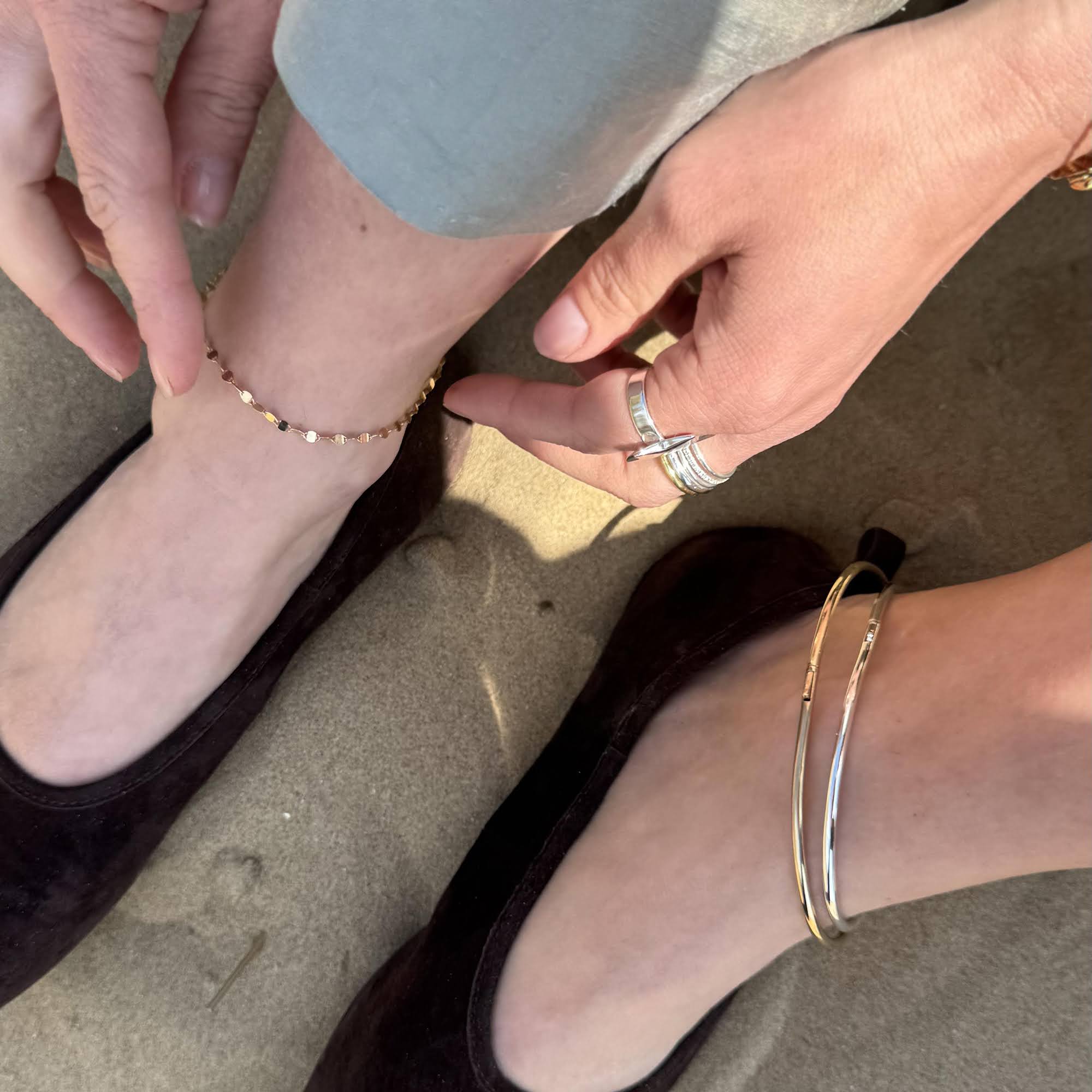 Close-up of a person's feet wearing gold anklets and a silver bracelet on a sandy surface - seolgold