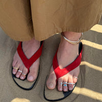 Red sandals worn on feet with beige pants on a sandy surface - seolgold