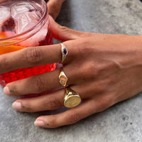 Hand wearing a gold ring with a purple gemstone, holding a red drink - seolgold