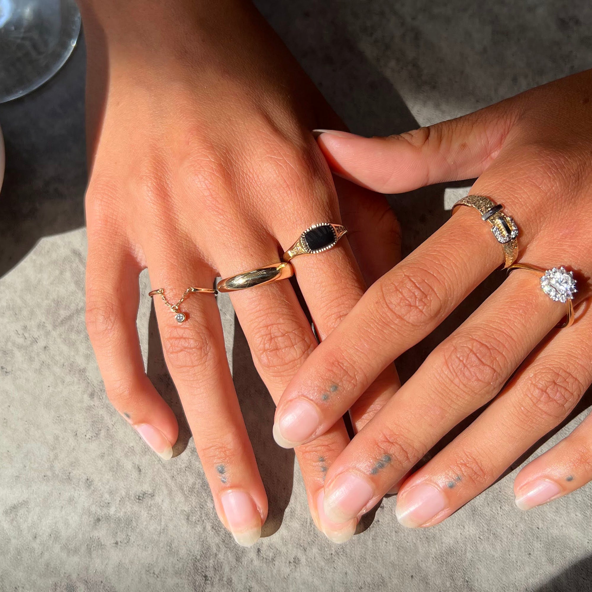 Close-up of hands wearing multiple rings on a neutral background - seolgold