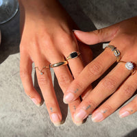 Close-up of hands wearing multiple rings on a neutral background - seolgold