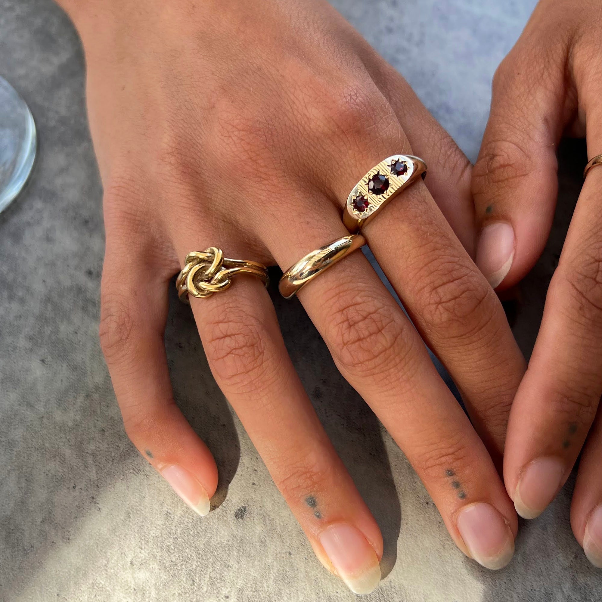 Close-up of hands wearing gold rings on a textured surface - seolgold