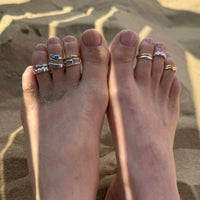 Feet with multiple rings on toes against a sandy background - seolgold