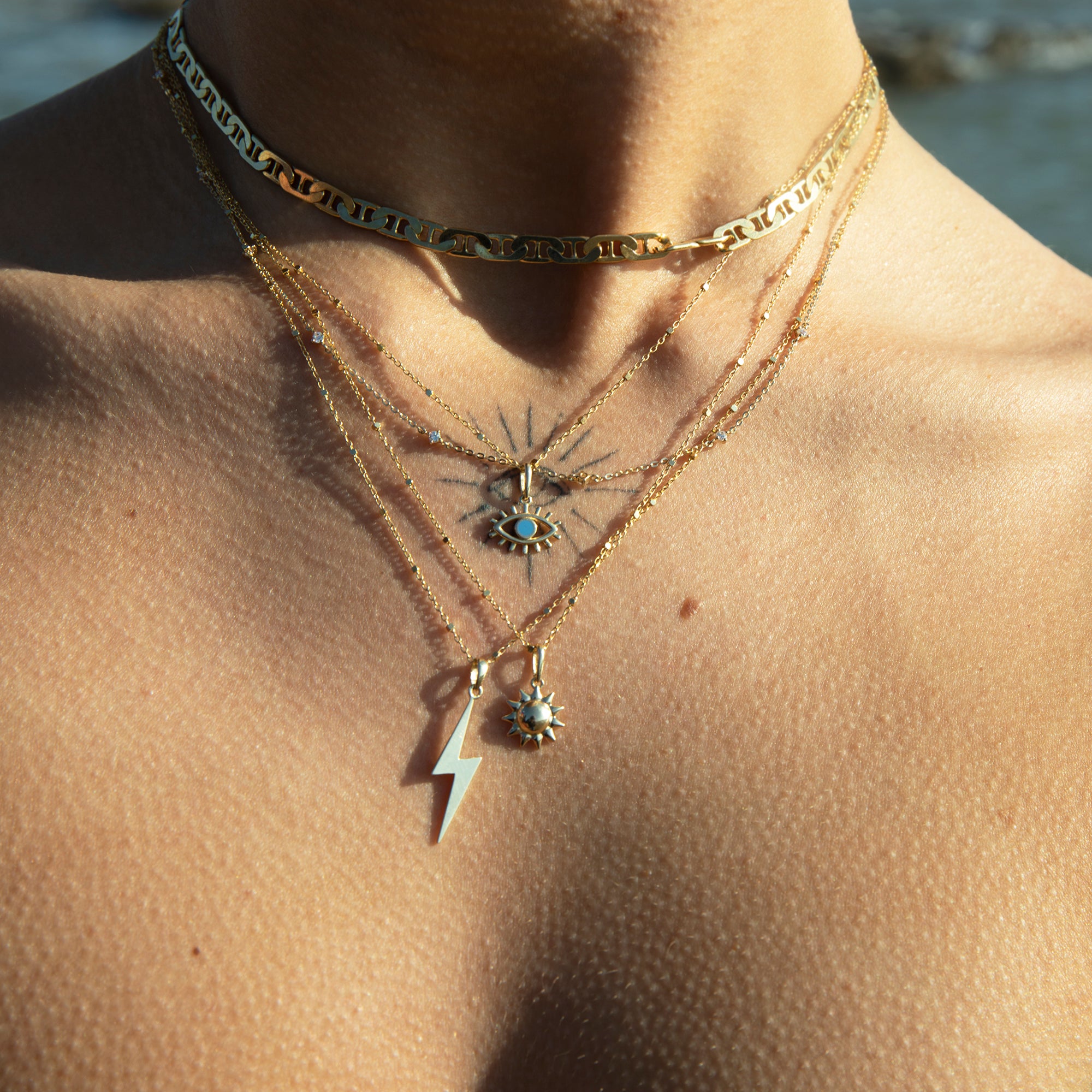 Close-up of a person wearing multiple gold necklaces with pendants against a blurred natural -background - 9ct Solid Gold Large Lightning Bolt Pendant - seolgold