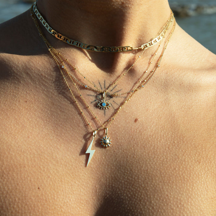 Close-up of a person wearing multiple gold necklaces with pendants against a blurred natural -background - 9ct Solid Gold Large Lightning Bolt Pendant - seolgold