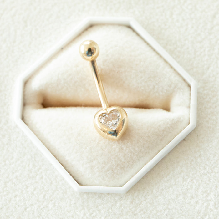 Gold belly button ring with heart design on a hexagonal white jewelry cushion - seolgold