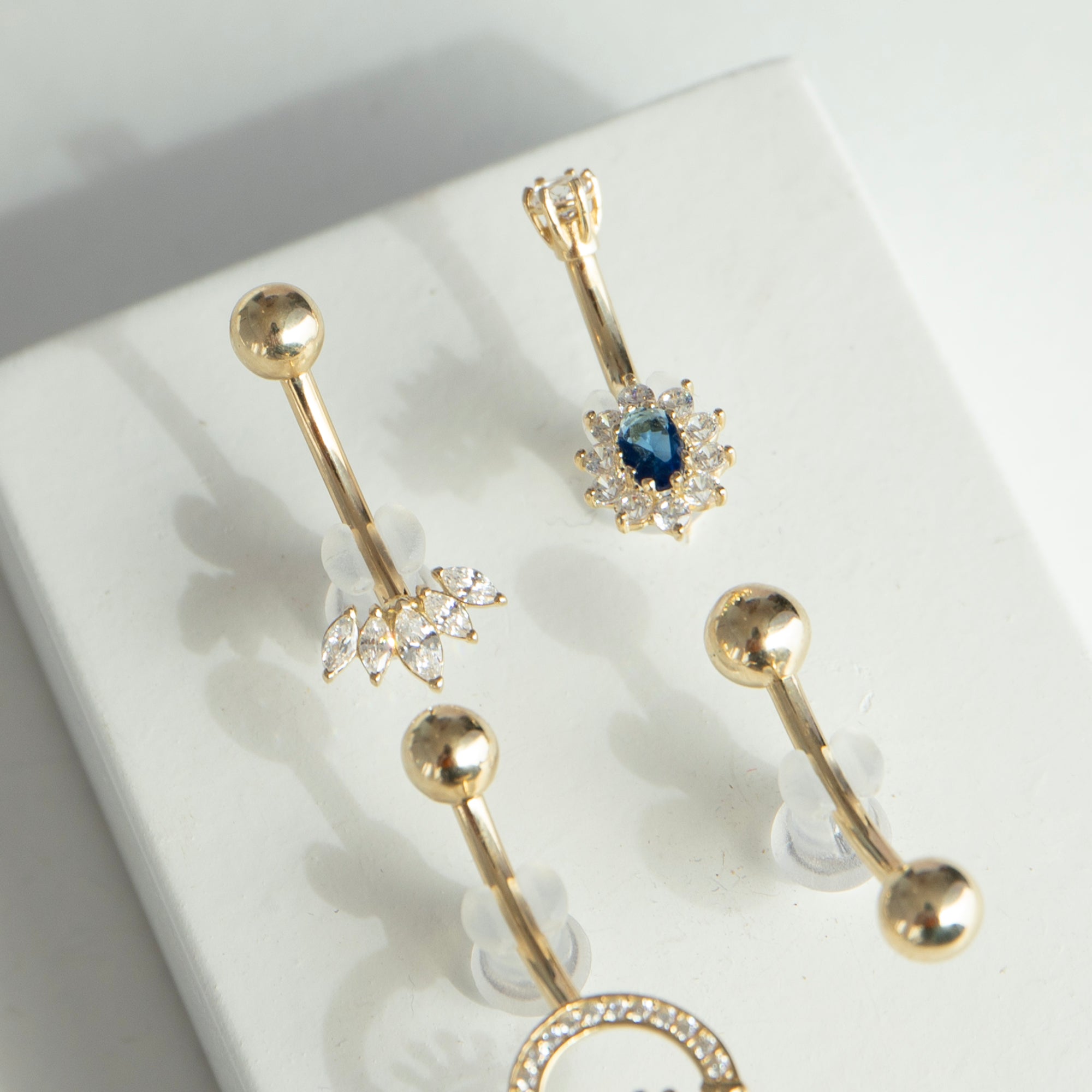 Gold belly button rings with sapphire gemstones on a white surface - seolgold