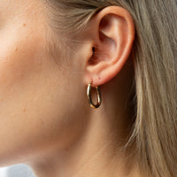 A close-up side profile of a woman's ear wearing a small gold hoop earring. Seol gold