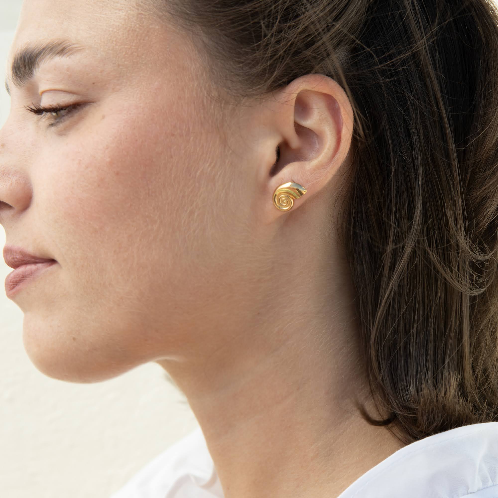 A close-up side profile of a woman wearing a small gold shell shaped stud earring - seolgold