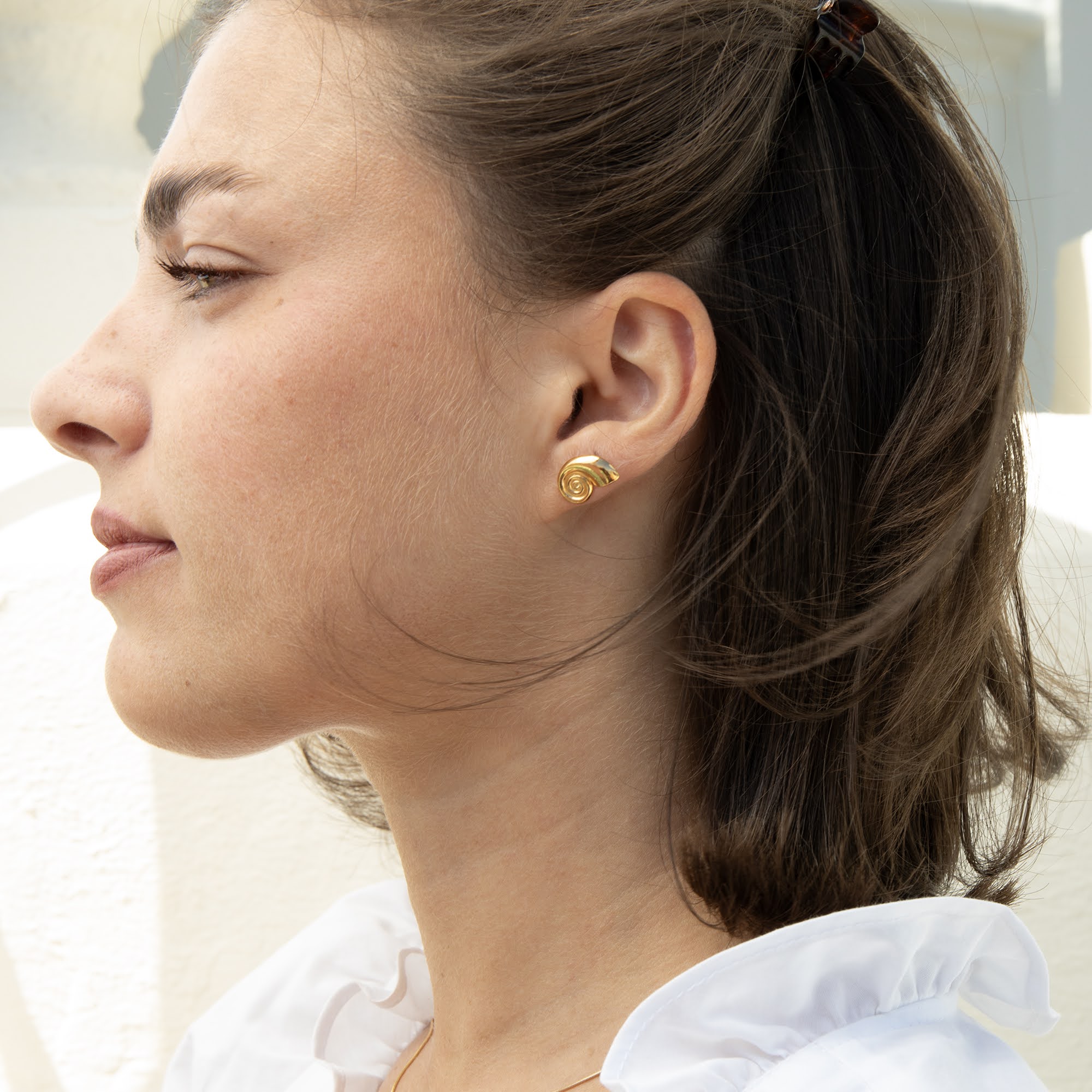 A close-up side profile of a woman wearing a small gold shell shaped stud earring - seolgold