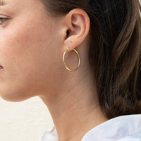 A close-up side profile of a woman wearing a thin gold hoop earring - seolgold