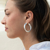 A close-up side profile of a woman wearing a large, rope twist silver hoop earring - seolgold