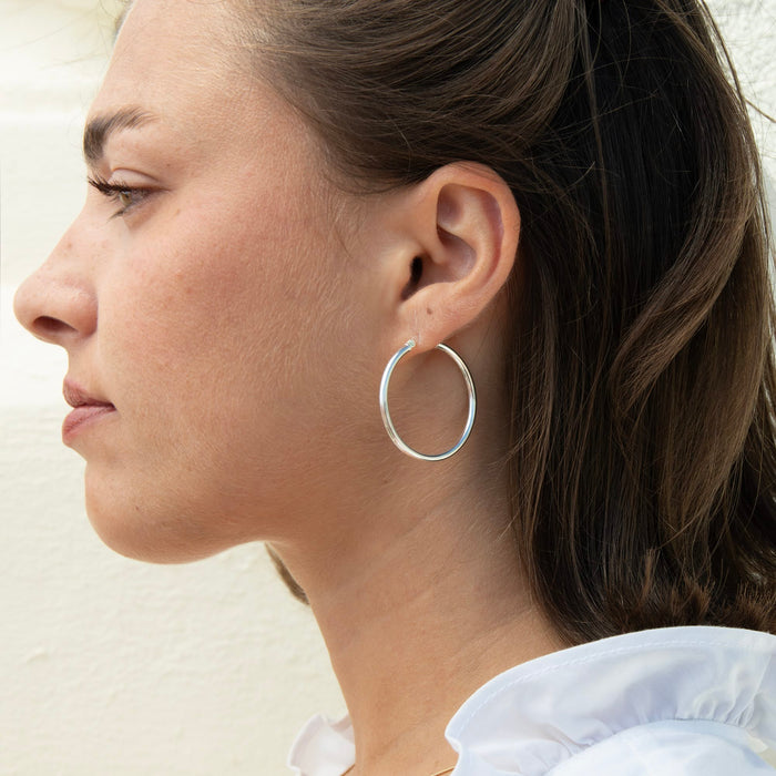 A close-up side profile of a woman wearing a large, thin silver hoop earring - seolgold
