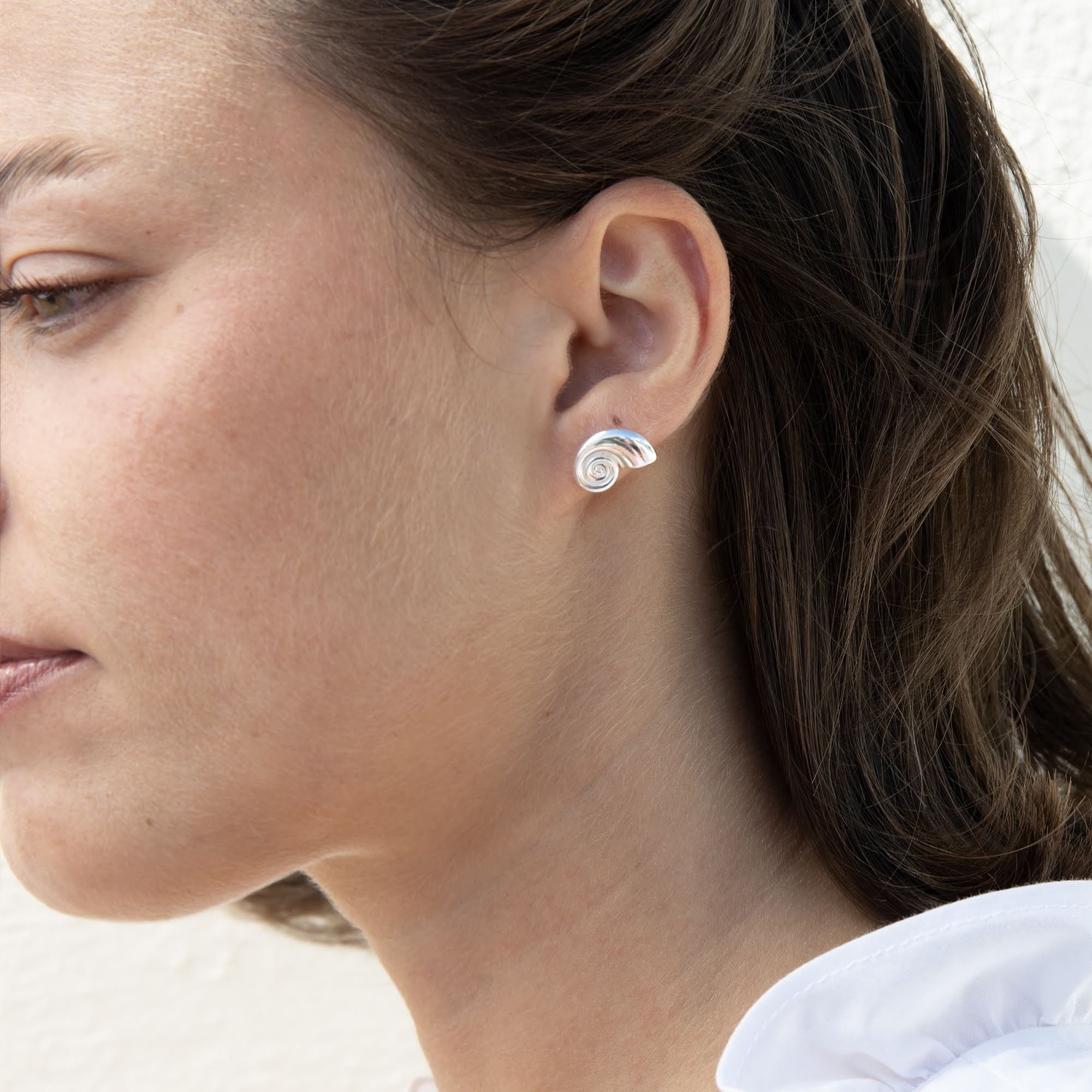 A close-up side profile of a woman wearing a small silver spiral stud earring - seolgold