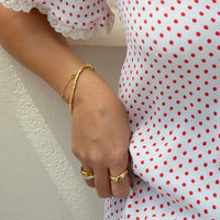 A close-up of a person's hand wearing delicate gold bracelets and rings, next to a white top with red polka dots - seolgold