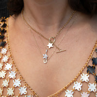 Close-up of a person's neck and chest wearing layered gold necklaces with celestial charms, including a star, ring, and crescent moon, over a white and gold patterned top - seolgold