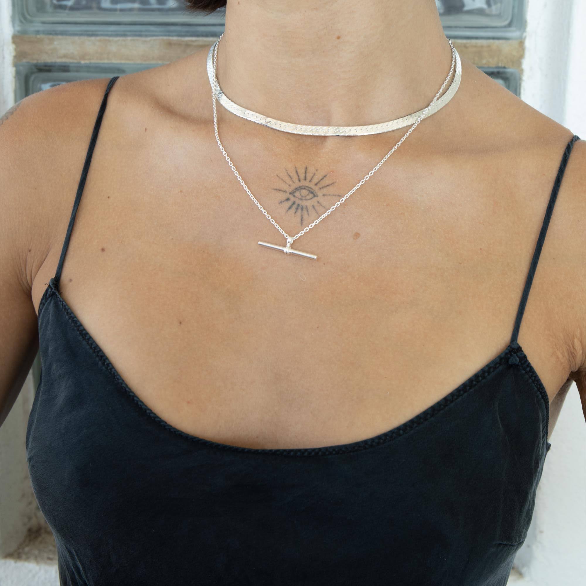 A close-up of a model's neck and chest wearing a layered silver necklace set, including a textured choker and a delicate chain with a bar pendant, styled with a black camisole top - seolgold