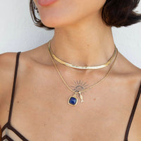 A close-up of a model wearing a layered gold necklace set. The top layer is a textured gold choker, and the bottom layer is a delicate gold chain featuring a square-cut dark blue pendant and a small gold key charm - seolgold