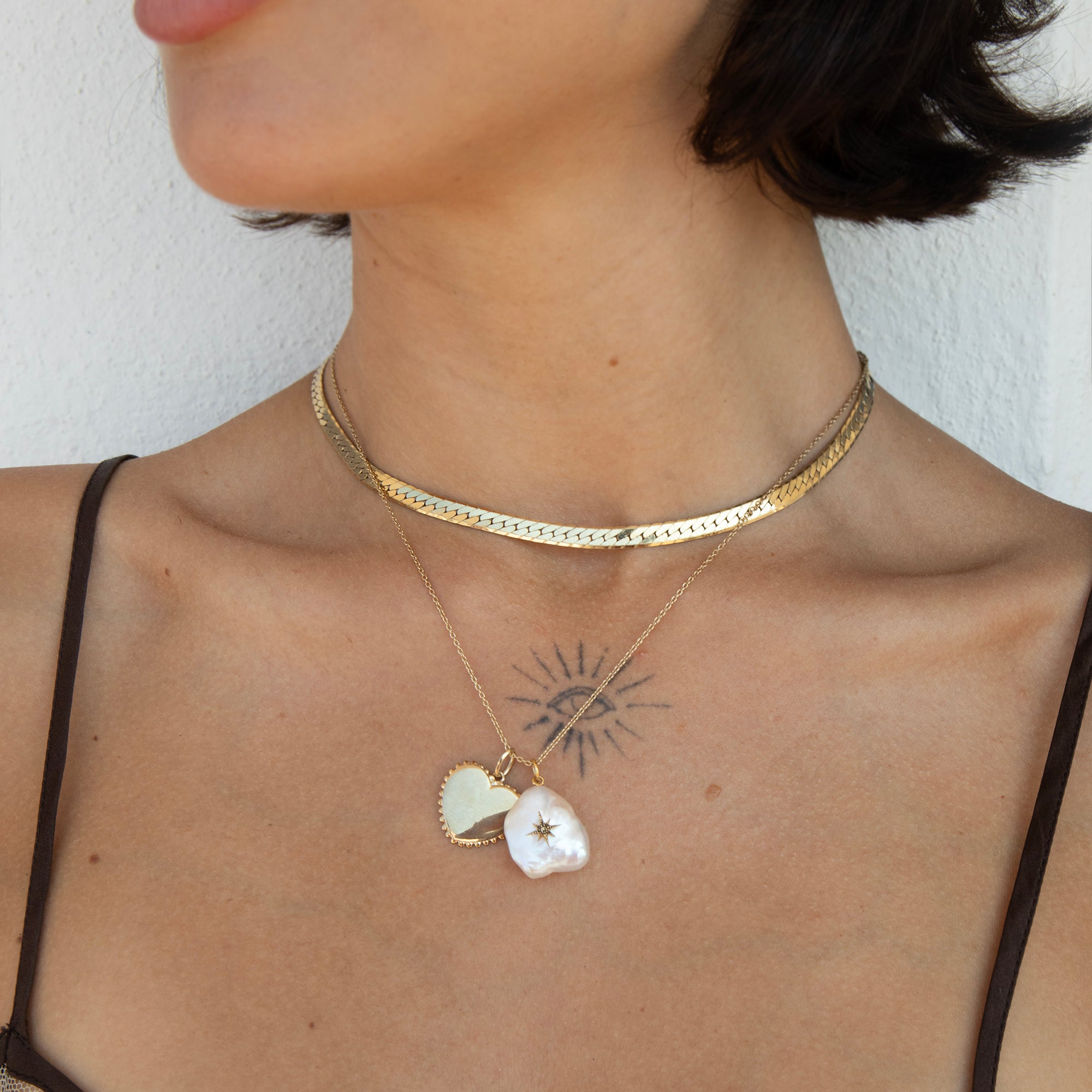 A close-up of a model's neck and chest wearing layered gold necklaces, including a textured choker and a delicate chain with two white shell pendants, one featuring a star detail - seolgold