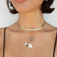 A close-up of a model's neck and chest wearing layered gold necklaces, including a choker with a textured band, a delicate chain with two pendants (one heart-shaped mirror, one white pearl with a star), and a thin chain with a sunburst pendant - seolgold