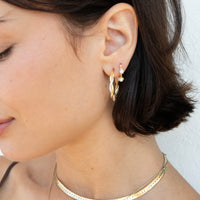 A close-up of a woman wearing a pair of gold hoop earrings with small white pearl accents, along with a gold chain necklace, against a plain white background - seolgold
