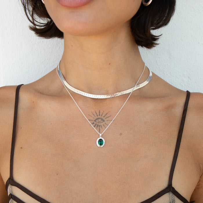 A close-up of a model wearing a layered necklace set featuring a textured silver choker, a fine silver chain with an eye pendant, and a silver chain with a green oval gemstone pendant - seolgold