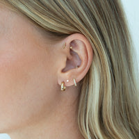 Close-up of a person's ear wearing multiple gold ear piercings and earrings, including hoop, stud, and cartilage piercings, against a light neutral background - seolgold