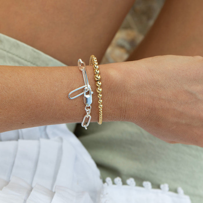 Two bracelets, one silver and one gold, on a person's wrist with a blurred background - seolgold