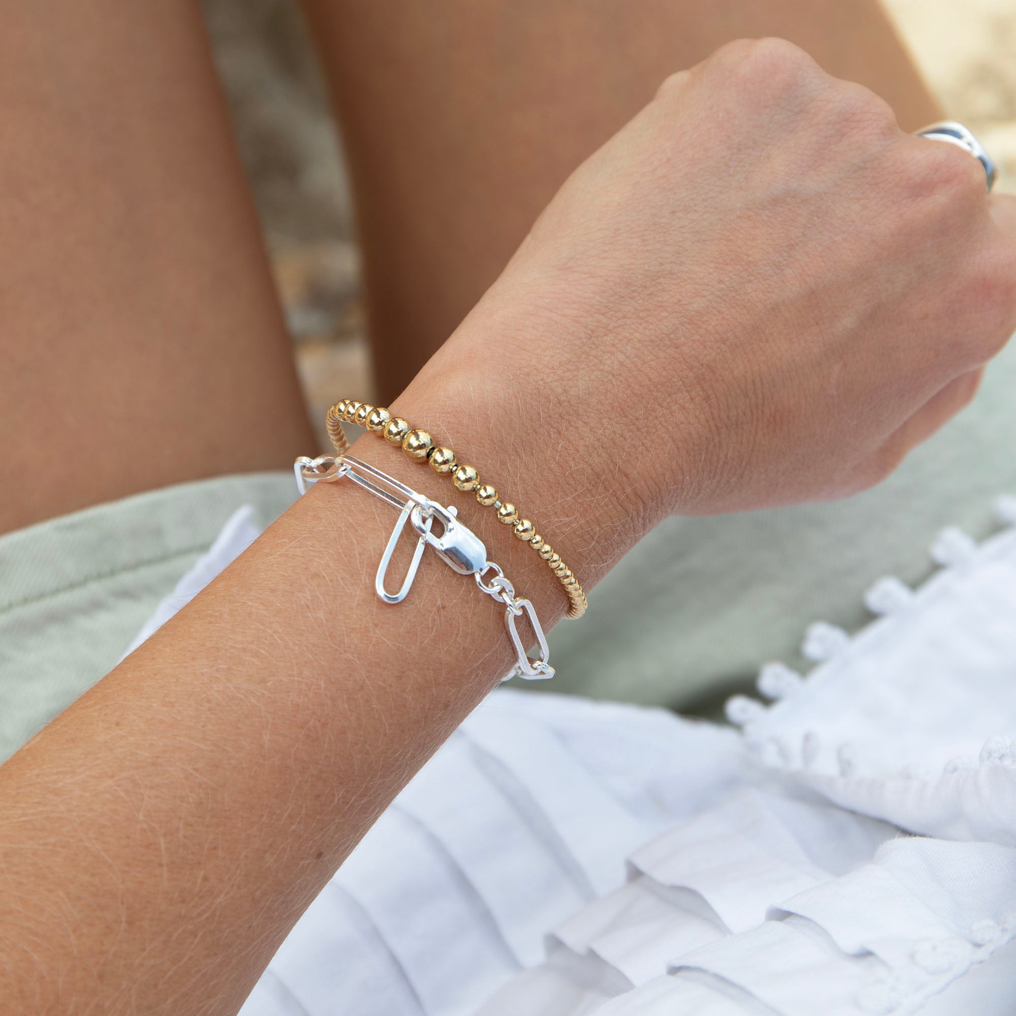 Close-up of a wrist wearing two bracelets with a blurred natural background - seolgold
