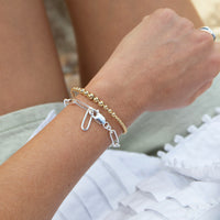 Close-up of a wrist wearing two bracelets with a blurred natural background - seolgold