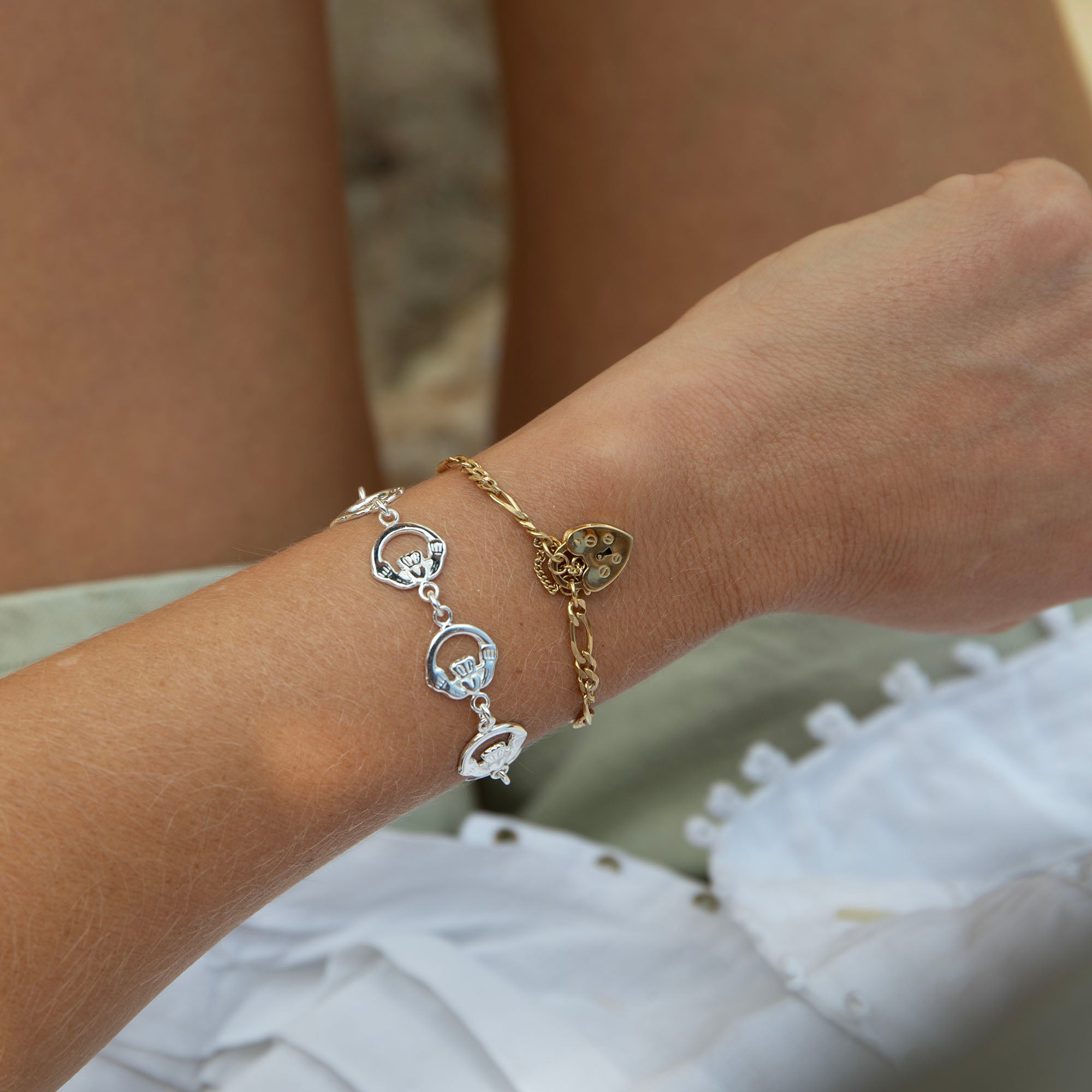Close-up of a wrist wearing two gold bracelets with heart and circular charms - seolgold