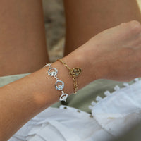 Close-up of a wrist wearing two gold bracelets with heart and circular charms - seolgold