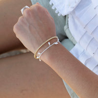 Close-up of a wrist wearing multiple bracelets with a blurred background - seolgold