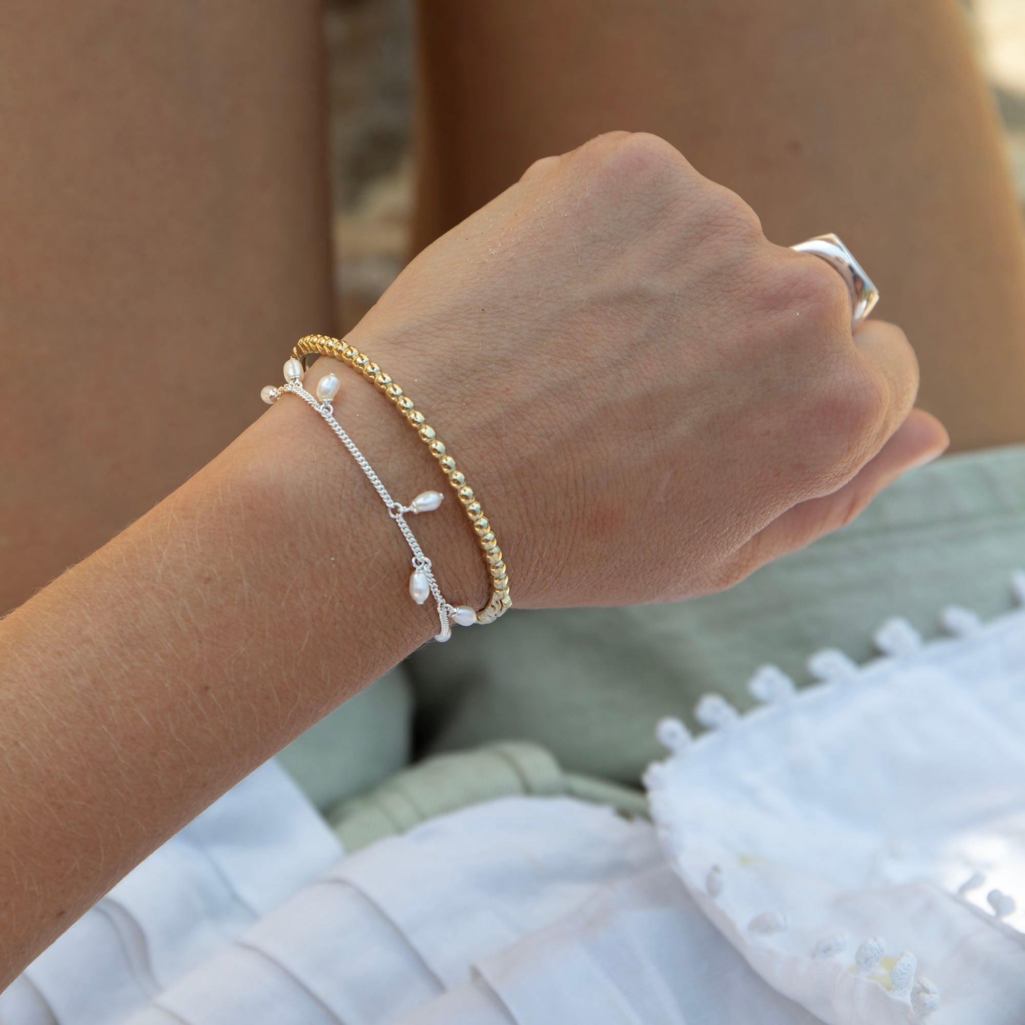 Close-up of a hand wearing gold and silver bracelets with pearls, sitting on a textured surface - seolgold