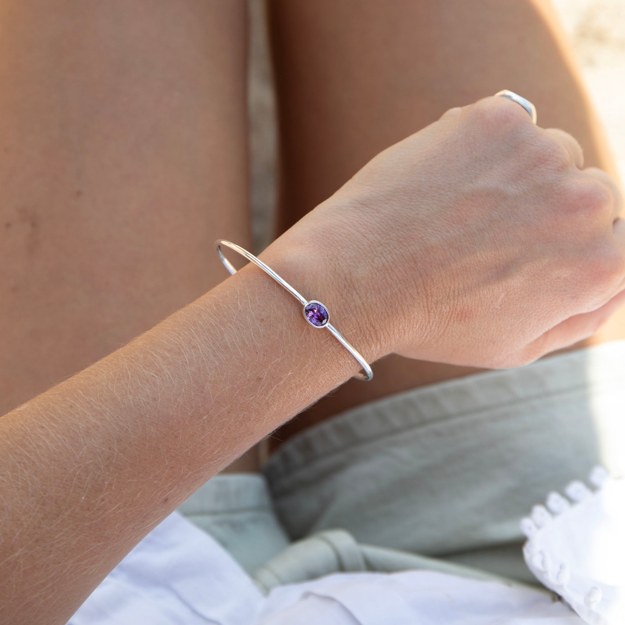 Silver bracelet with a purple gemstone on a wrist against a neutral background - seolgold
