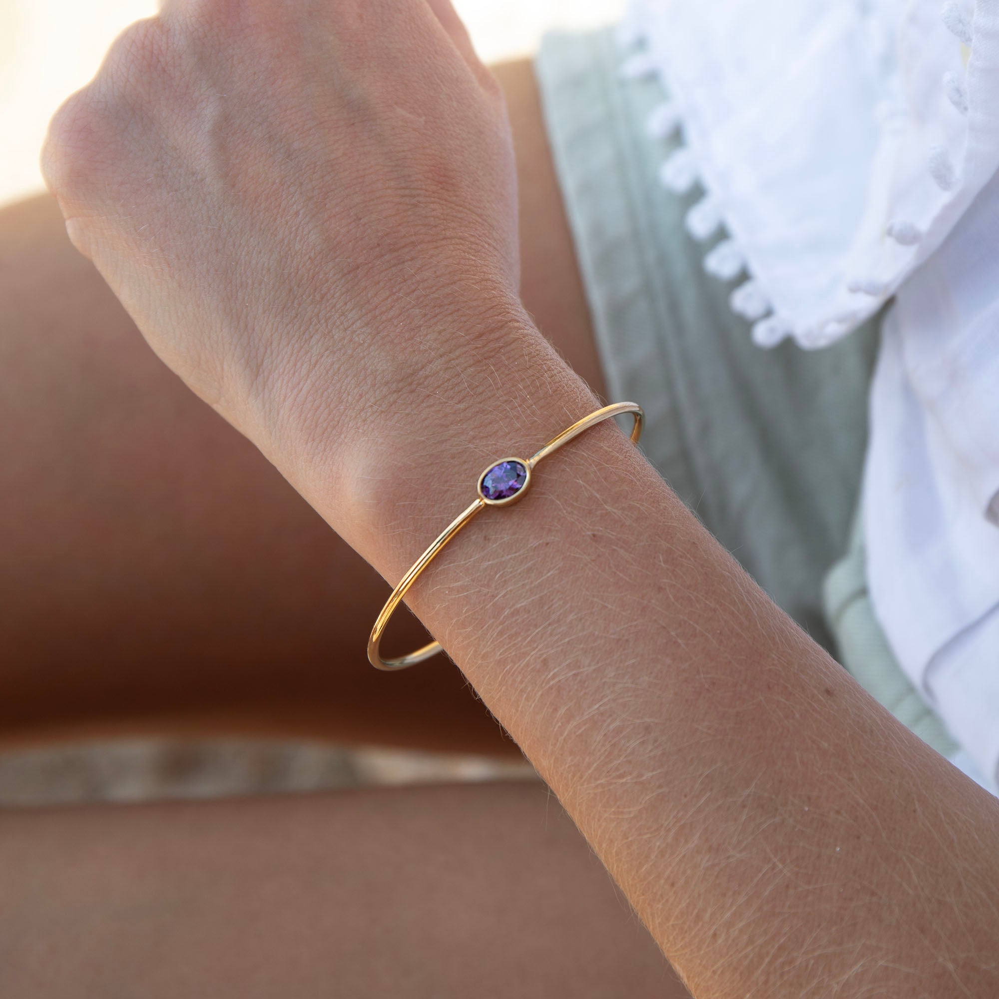 Gold bracelet with a purple gemstone on a wrist against a blurred background - seolgold