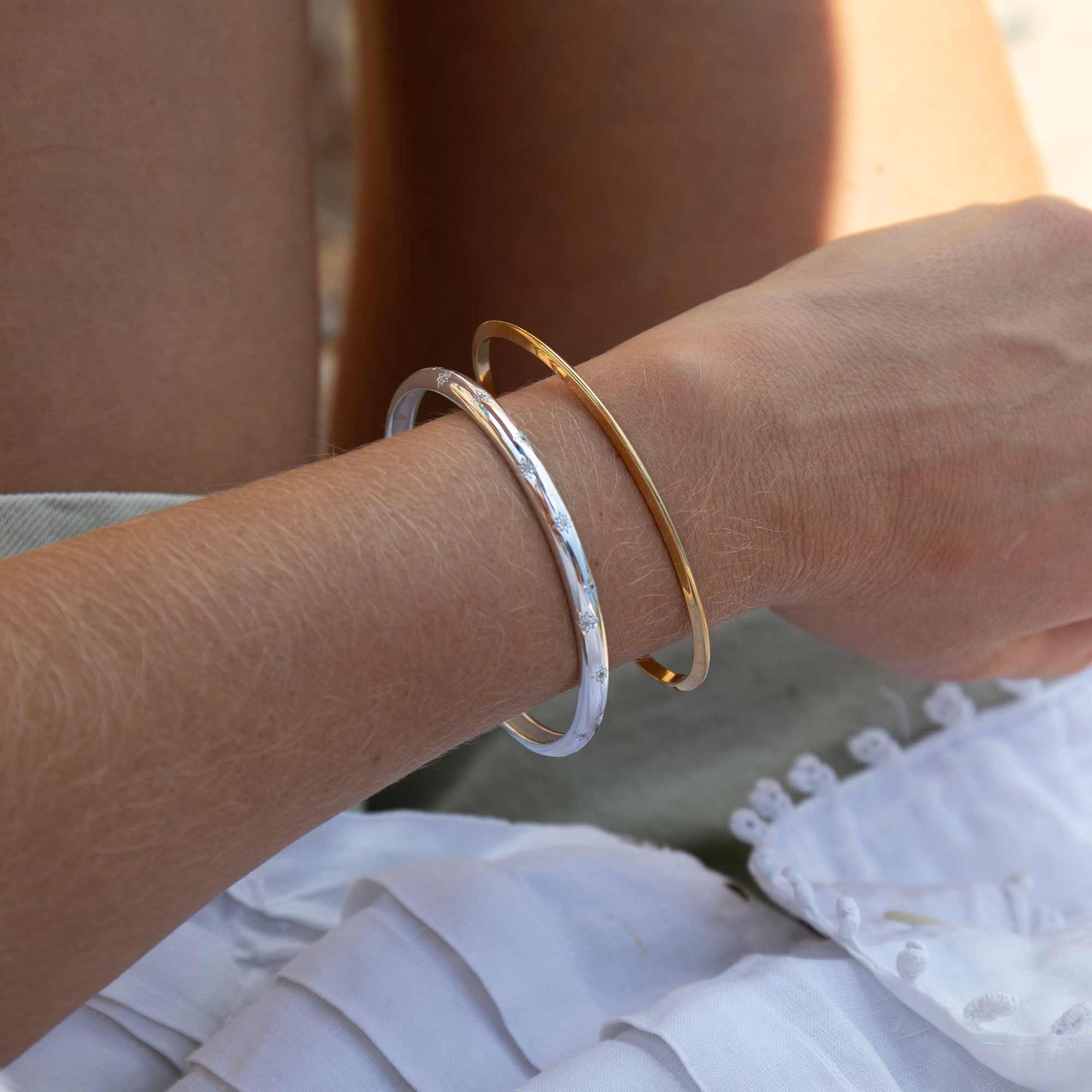 Close-up of a person's arm wearing two bracelets, one gold and one silver, with a blurred background - seolgold