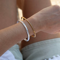 Close-up of a wrist wearing two bracelets, one gold and one silver, against a neutral background - seolgold