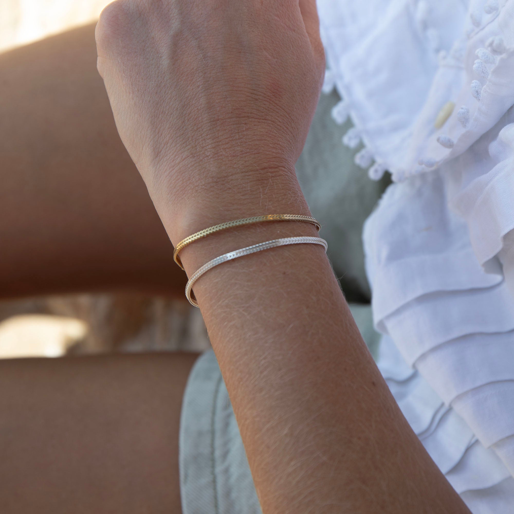 Close-up of a wrist wearing two gold bracelets with a blurred background - seolgold