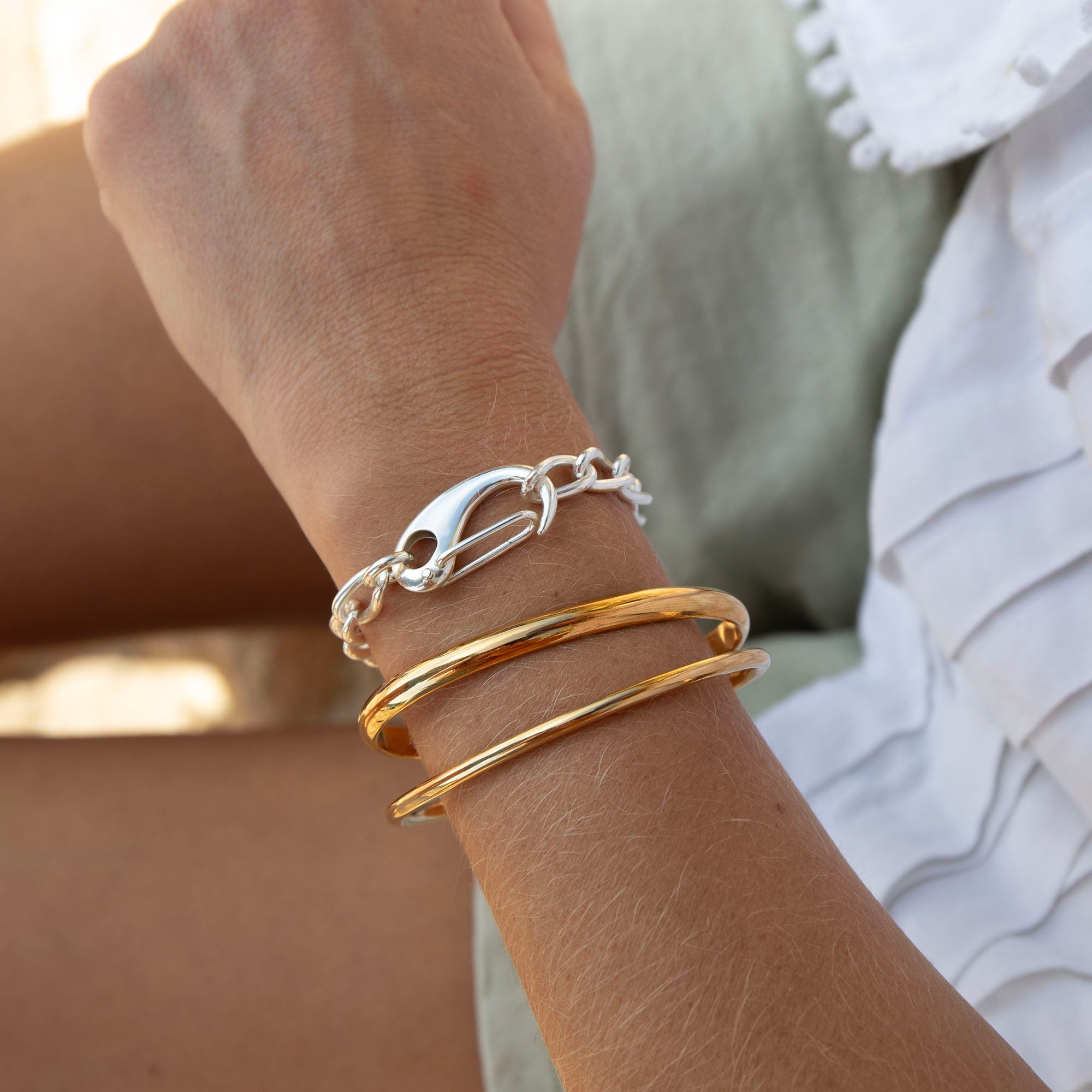 Close-up of a wrist wearing gold and silver bracelets with a blurred background - seolgold