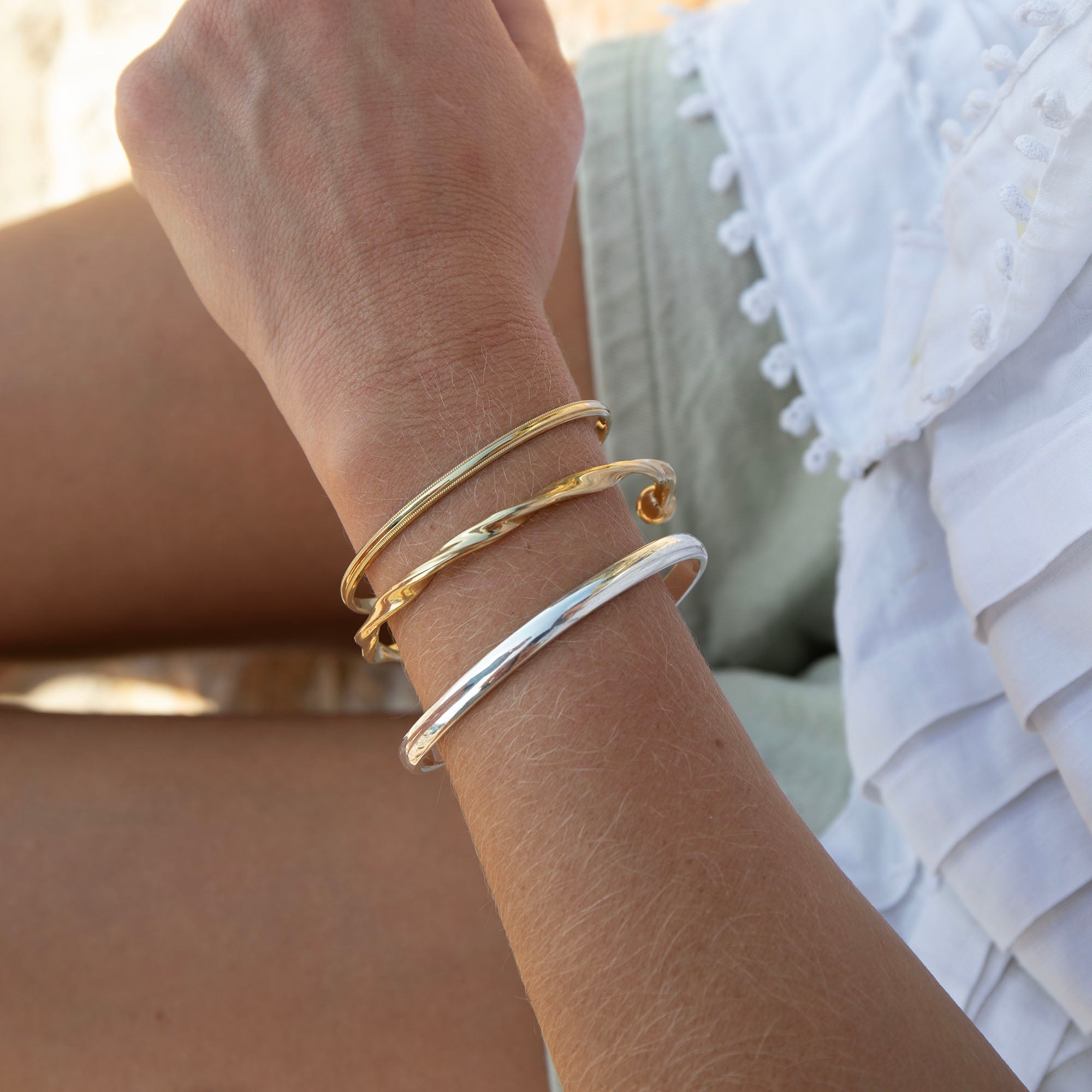 Close-up of a wrist wearing gold bracelets with a blurred background - seolgold