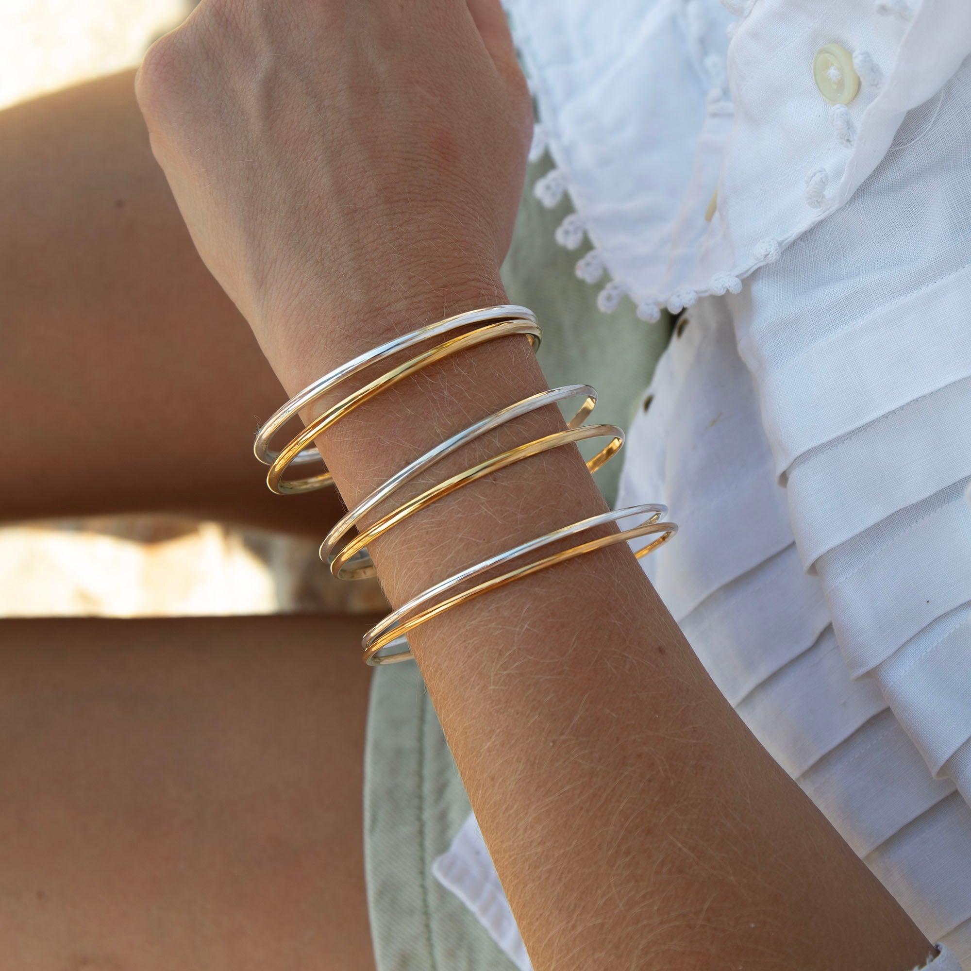 Close-up of a wrist wearing gold bracelets with a blurred background - seolgold