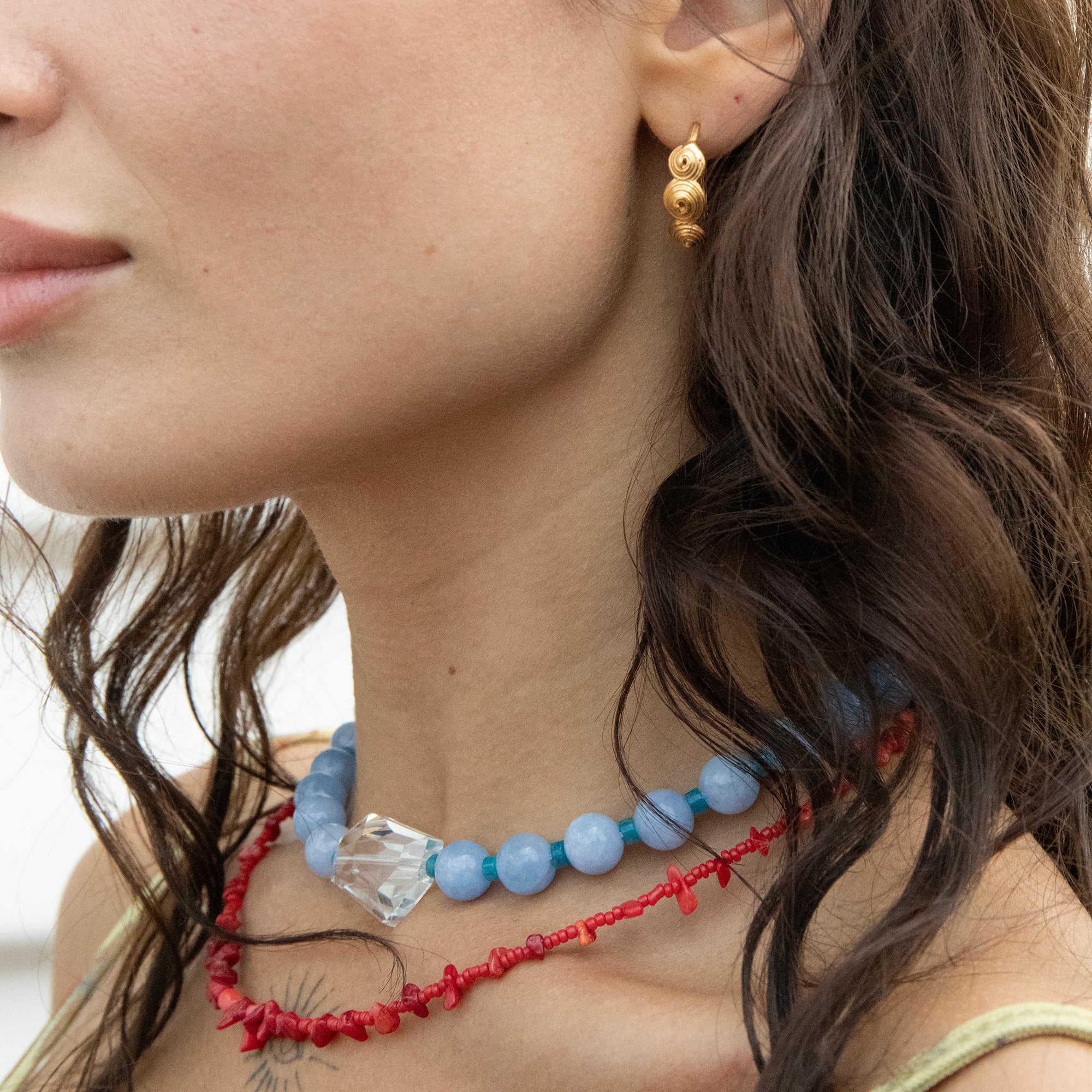 Close-up of a woman wearing a blue beaded necklace and gold earrings with a blurred background - seolgold