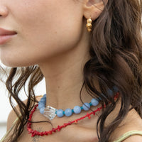 Close-up of a woman wearing a blue beaded necklace and gold earrings with a blurred background - seolgold
