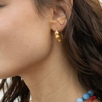 Close-up of a person wearing gold earrings with a blurred background - seolgold