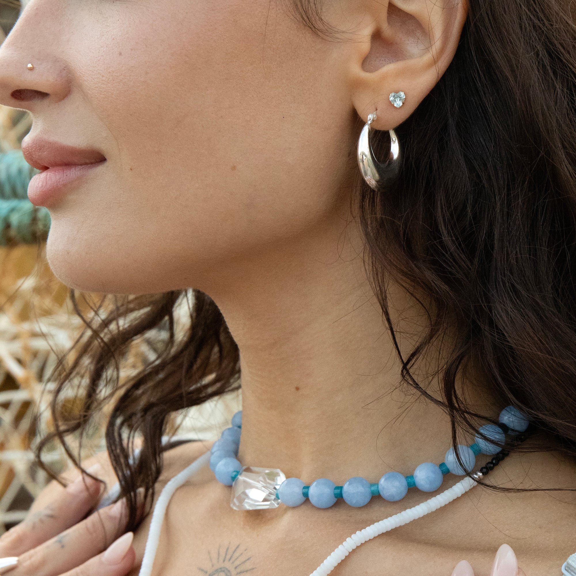 Close-up of a woman wearing a blue beaded necklace and silver earrings with a blurred natural background - seolgold