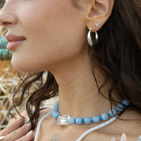 Close-up of a woman wearing a blue beaded necklace and silver earrings with a blurred natural background - seolgold