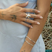 Close-up of a hand wearing a starfish ring and silver bracelet with a neutral background - seolgold